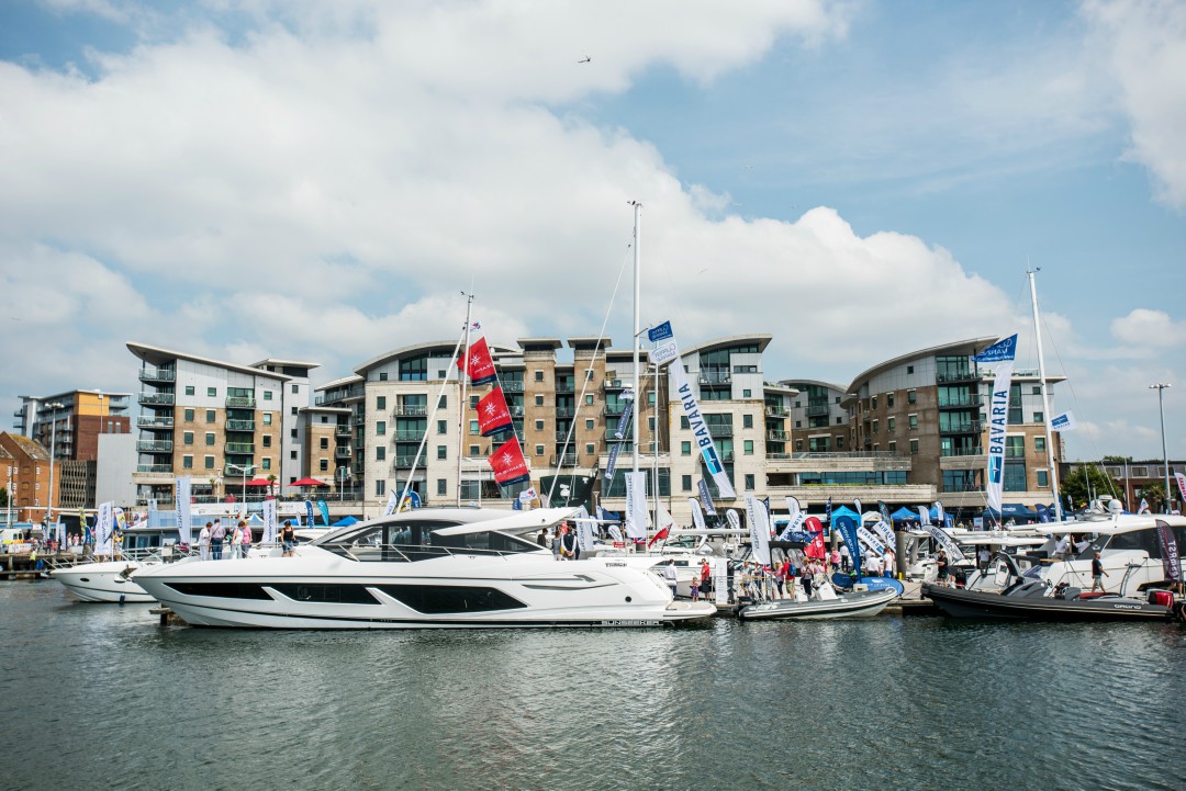 A yacht sits prominently in Poole Harbour over the weekend of the Boat Show, with a crowd milling in the background